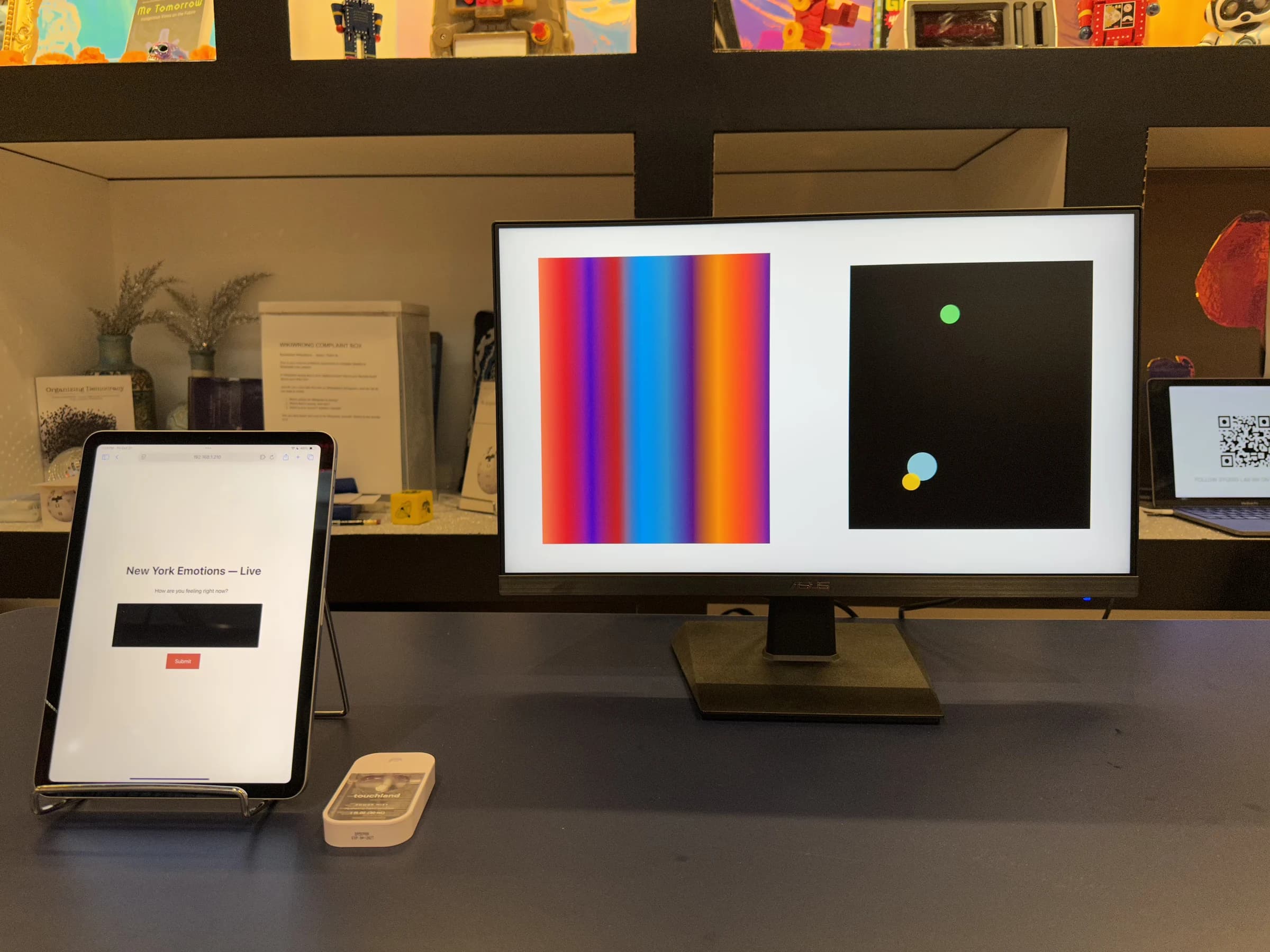 An iPad asks how visitors feel beside a monitor showing a daily color field and three colored circles.